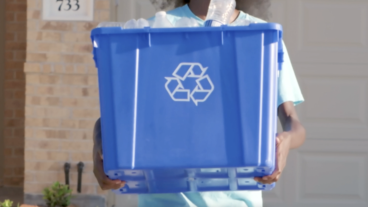 A person holding a blue recycling bin with plastic water bottles in it.